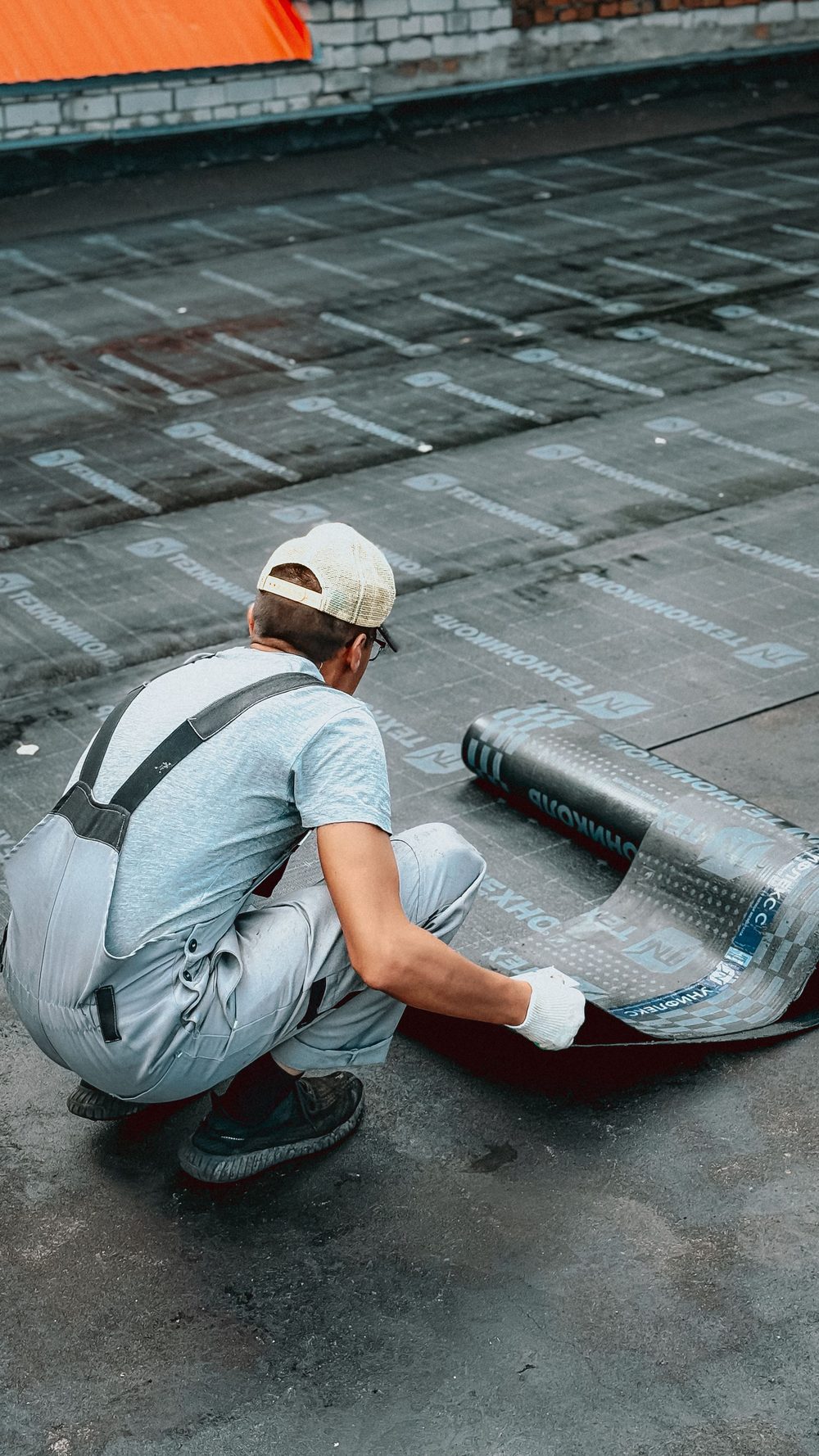 Roofer unrolling a modified bitumen membrane across a flat roof
